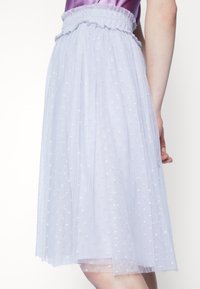 Jupe en tulle violet clair avec une ceinture smockée, ornée de motifs d'étoiles blanches sur l'ensemble et un design superposé et fluide.