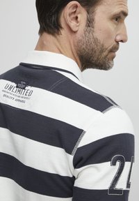 Polo a rayas en navy y blanco con mangas cortas, un cuello y un destacado aplique de 24 en la manga derecha. Tejido texturizado con detalles de costura.