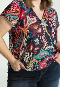 Top de manga corta y escote en forma de V con un colorido estampado de paisley sobre un fondo oscuro, hecho de una tela texturizada. Presenta diversas tonalidades de rosa, azul y verde.
