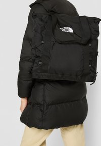 Mochila negra hecha de un tejido duradero, con una tapa plegable, correas ajustables, detalle con logotipo y superficie texturizada.