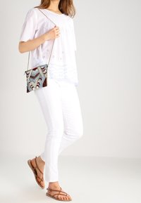 Hvid, broderet bluse med korteærmer, parret med tætsiddende hvide jeans og brune sandaler med stropper. Accessoriseret med en tekstureret mønstret taske.