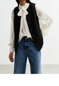 Černá vesta s pěti kulatými knoflíky, nošená přes bílou blůzu s mašlí. Vybaveno s modrými širokými džíny.