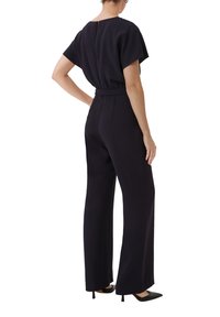 Schwarzer Jumpsuit mit entspannter Passform, kurzen Ärmeln und tailliertem Bund. Mit weitem Bein und einem Reißverschluss auf der Rückseite. Glatte Stofftextur.