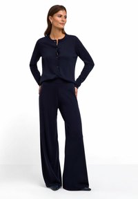 Navyblaues Strickcardigan mit Rundhalsausschnitt und Knopfverschluss, kombiniert mit einer weit geschnittenen Hose. Glatte Textur und eine lockere Passform.