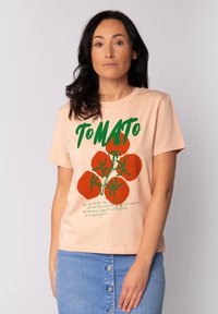 Pfirsichfarbene Baumwoll-T-Shirt mit grüner "ToMATO"-Schrift und roten Tomatengrafiken mit grüner Ranke, kombiniert mit einem Jeansrock. Einfaches, lässiges Design.