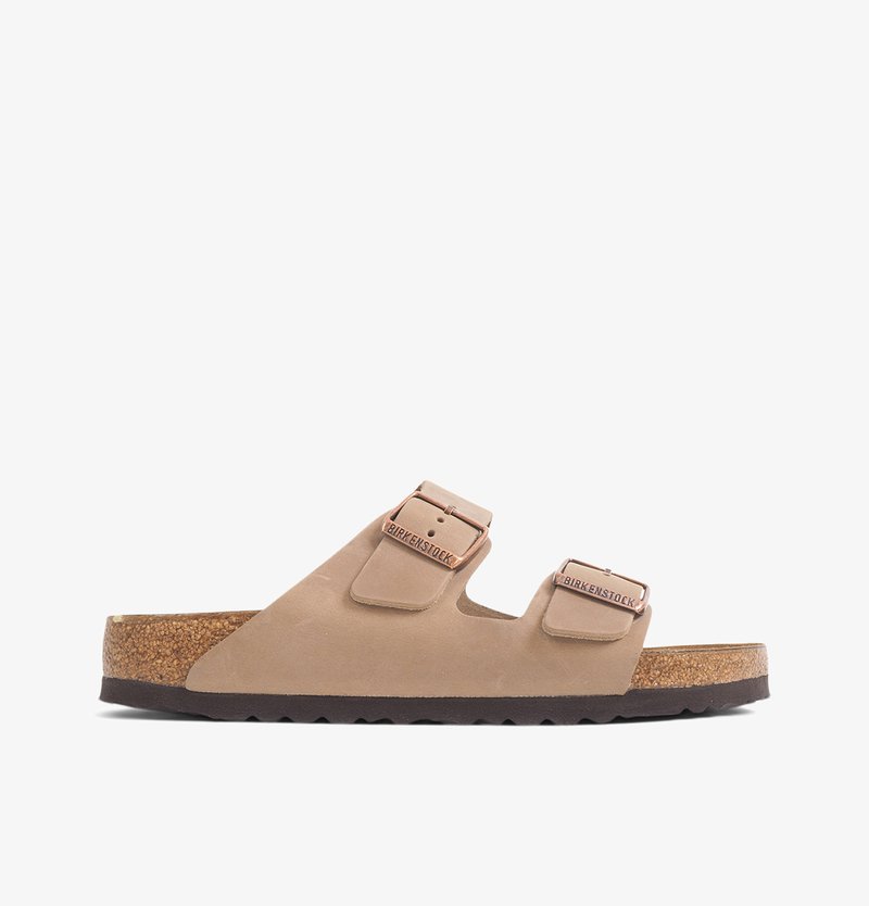 Sandalia de dos bandas en piel beige clara con plantilla de corcho, hebillas metálicas ajustables y suela texturizada para un mayor agarre.