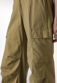 Pantaloni cargo verde oliva realizzati in tessuto leggero e strutturato, caratterizzati da tasche laterali e dettagli di design plissè.