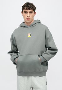 Γκρι φούτερ με κουκούλα και τσέπη καγκουρό, με πολύχρωμο λογότυπο στο στήθος. Κατασκευασμένο από μαλακό ύφασμα με ριμπ τελειώματα στα μανίκια και στο κάτω μέρος.