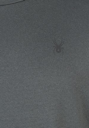 Tejido texturizado gris oscuro con un sutil patrón tejido. Presenta un pequeño logotipo de araña negra en la zona del pecho.