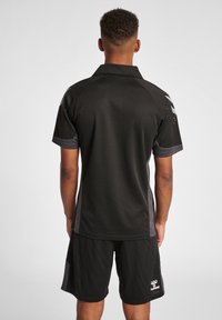 Sort sports polo med grå accenter; korte ærmer, krave, mesh tekstur. Bæres med matchende sorte shorts med logo-detalje.