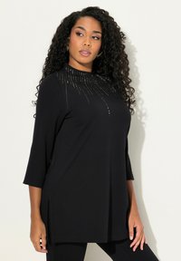 Tunic nera con maniche a tre quarti, caratterizzata da un design del collo con borchie, fessure laterali e una vestibilità ampia e rilassata. Tessuto dalla texture morbida.