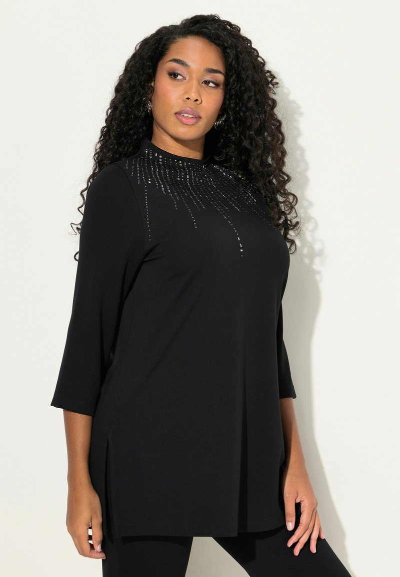 Tunic nera con maniche a tre quarti, caratterizzata da un design del collo con borchie, fessure laterali e una vestibilità ampia e rilassata. Tessuto dalla texture morbida.