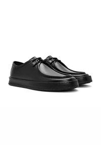 Zapatos de cuero negro con un acabado suave, punta redondeada, diseño con cordones y suela gruesa con detalles de costura.