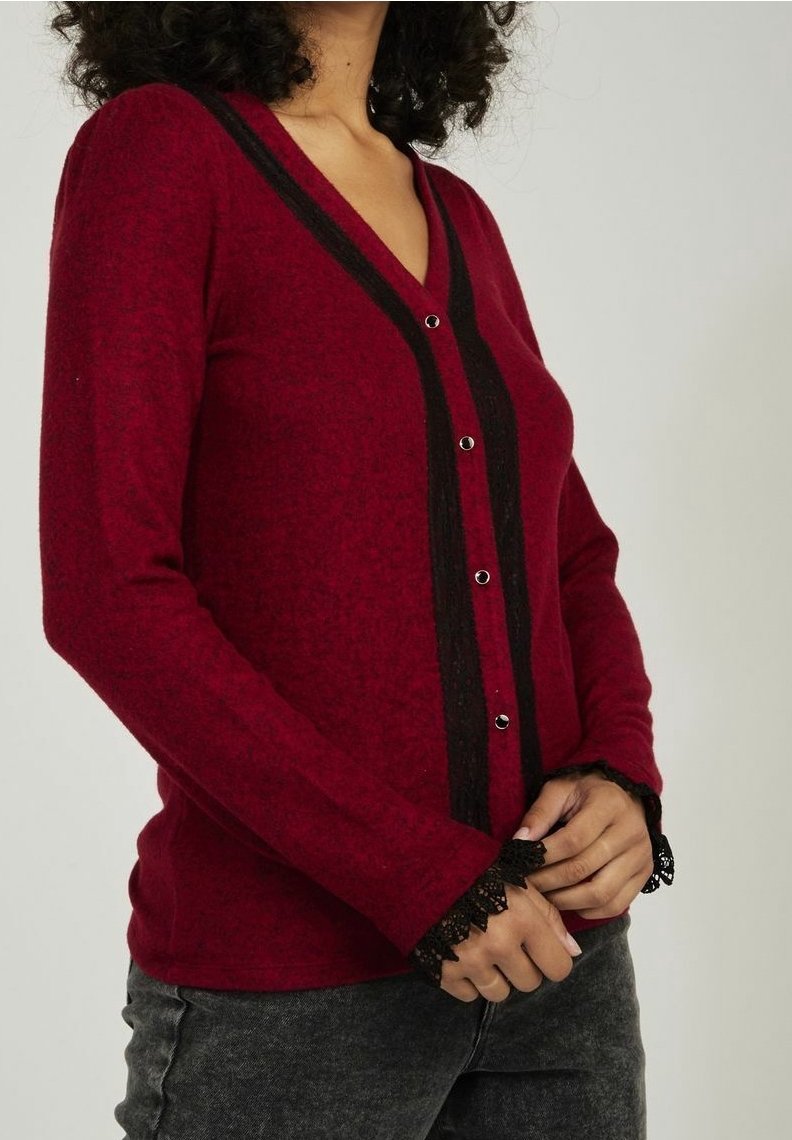 Czerwony kardigan z długim rękawem, z dekoltem w serek, czarnymi paskami na środku i koronkowym wykończeniem przy mankietach; posiada srebrne guziki z przodu.