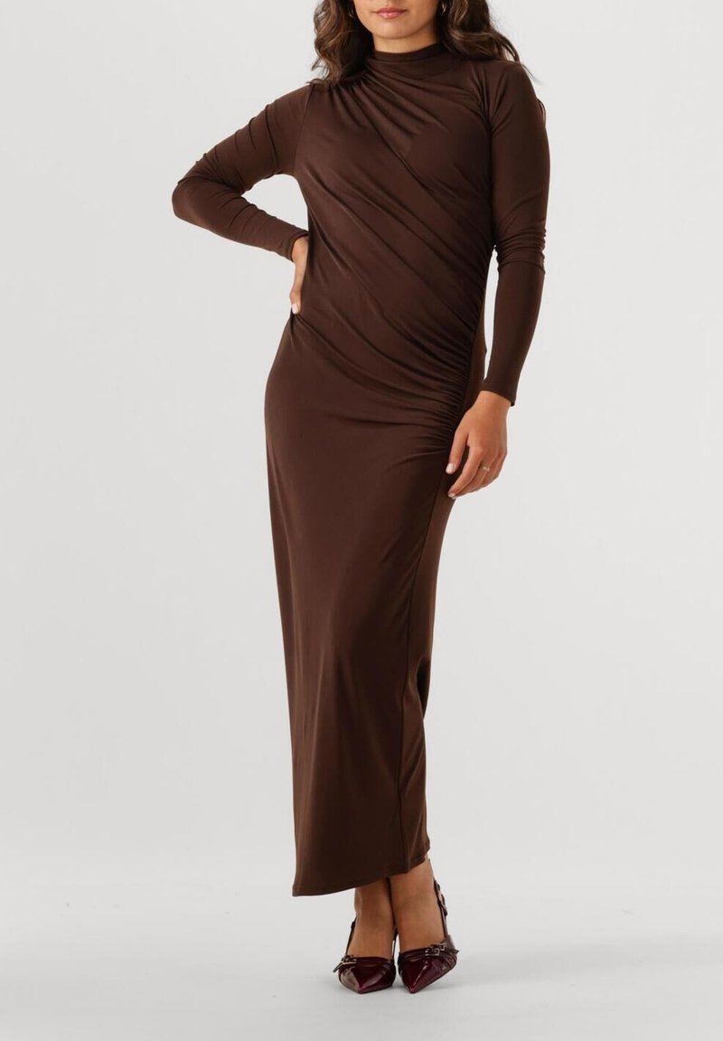 Robe longue marron à manches longues avec un col montant, présentant des détails drapés et une fente sur le côté. Tissu lisse et extensible qui améliore l'ajustement et le mouvement.