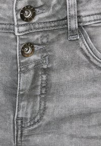 Primo piano di jeans in denim grigio con bottoni metallici etichettati "STREET," tasca visibile e dettagli di cucitura del passante della cintura.
