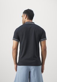 Svart polo skjorte med hvite detaljer, teksturert stoff og en kontrastlogodetalj på baksiden, sammen med lyseblå shorts.