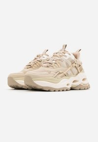 Par beige og creme chunky sneakers med tykke såler, mesh- og læderpaneler samt trækstropper på en hvid baggrund.