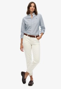 Blauw en wit gestreepte overhemd met knopen, witte broek, bruine gevlochten riem en donkerrode loafers, met een casual, nauwsluitend ontwerp.