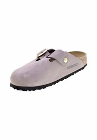 Zoccolo Birkenstock in morbida suede lavanda, con punta rotonda, singolo cinturino con fibbia in ottone, suola in sughero e suola esterna nera texturizzata.