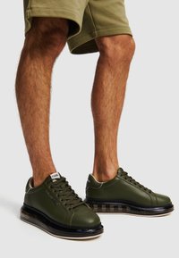 Sneaker in pelle verde con punta arrotondata, suola traslucida nera e suola intermedia imbottita. Presenta lacci frontali e dettagli a contrasto.