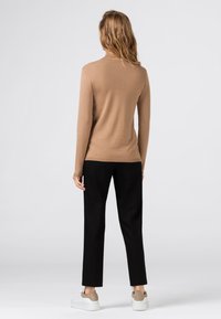 Béžový přiléhavý rolákový svetr, lehký úplet, dlouhé rukávy. Kombinováno s černými kalhotami a bílými teniskami, zobrazen zezadu.