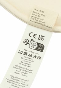 Cotton cream label with care instructions attached to a soft foam product. Includes text and recycling icons, sewn edges, and certification marks.