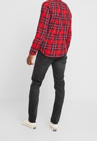 Camicia a quadri rossi e blu con maniche lunghe, orlo curvo, polsini con bottoni e jeans neri; indossata con sneakers bianche.
