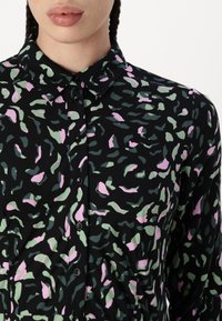 Chemise noire à boutons avec un motif fluide de formes vertes et roses, fabriquée en tissu doux, avec un col et des manches longues.