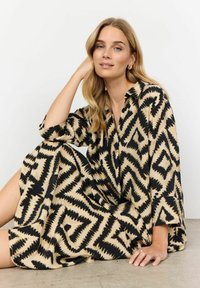 Lange jurk in een zwart en beige zigzagpatroon. Gemaakt van zachte stof, met een kraag en losse mouwen.