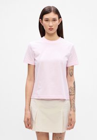 Lys pink kortærmet t-shirt lavet af bomuld. Har en rund hals og et trykt logo i en lidt mørkere nuance. Glat tekstur.