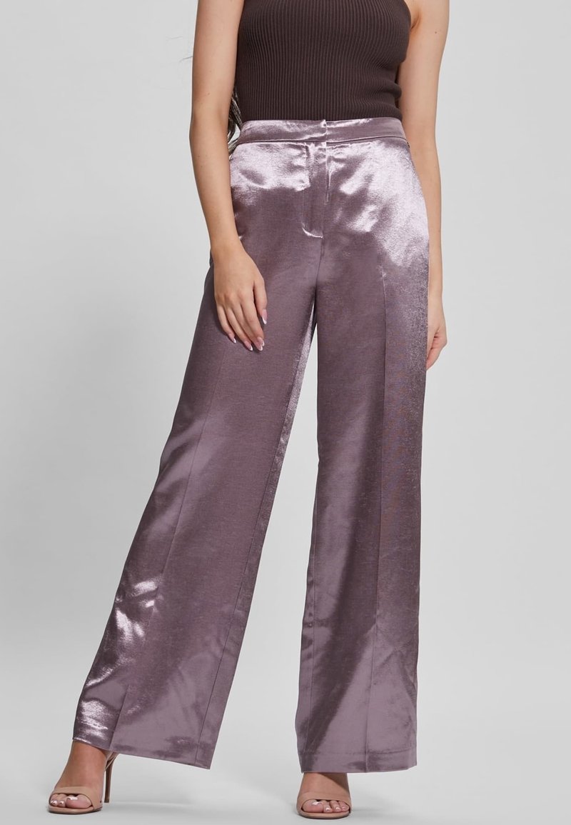 Femme portant un pantalon large en satin lavande brillant avec des fentes latérales, associé à un haut côtelé sans manches marron foncé et des talons couleur nude.