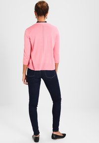 Różowy sweter dziany z rękawami do łokcia, teksturowany tył, zestawiony z ciemnymi, dopasowanymi dżinsami i czarnymi balerinami.