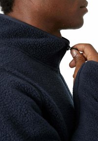 Navy fleece pullover with a high collar, featuring a zip closure and textured fabric. The cuff is slightly loose with a soft finish.
