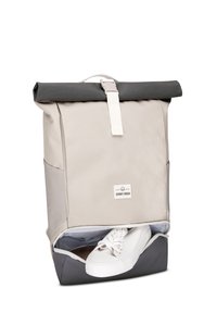 Beige és szürke szövetből készült roll-top hátizsák, fehér pánttal és hardverrel. Cipőtartó rekesszel rendelkezik, látható fehér tornacipőkkel.