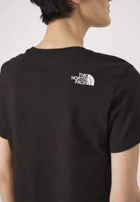 Black cotton t-shirt with short sleeves, featuring a white logo on the upper back. Classic crew neck design, smooth texture.