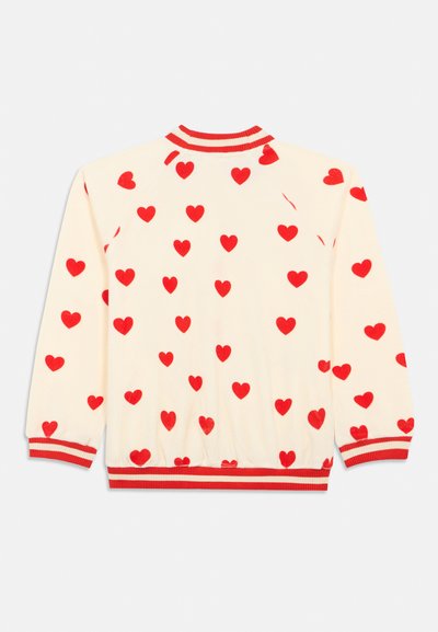 Suéter de manga larga crema con patrón de corazones rojos, cuello, puños y cinturilla a rayas rojas y crema visibles desde la parte de atrás.