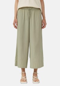 Pantalons larges vert clair en tissu doux avec une taille élastique et un cordon de serrage, présentant une coupe décontractée et des fentes latérales.