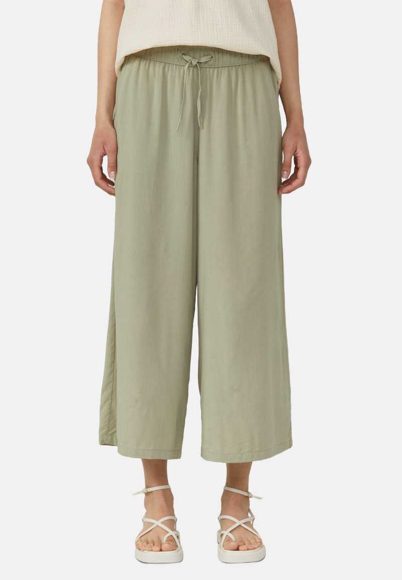 Pantalons larges vert clair en tissu doux avec une taille élastique et un cordon de serrage, présentant une coupe décontractée et des fentes latérales.