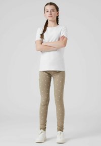 Leggings beige lunghi con piccoli motivi floreali bianchi, abbinati a una maglietta bianca a maniche corte e sneakers bianche.