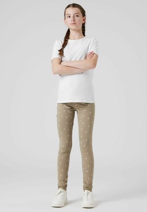 Lange beige Leggings mit kleinen weißen Blumenmustern, kombiniert mit einem schlichten weißen T-Shirt mit kurzen Ärmeln und weißen Turnschuhen.