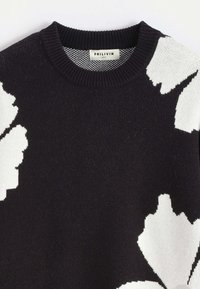 Pull noir avec de grands motifs floraux abstraits blancs, col rond côtelé, et étiquette de marque visible "FRILIVIN" taille M.