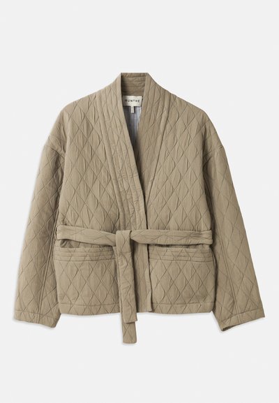 Beige kviltjakke med belte i midjen, lange ermer og diagonalt sømmermønster. Har sidelommer og sjalkrage.