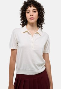 Polo à manches courtes en crème avec un col classique, patte de boutonnage à cinq boutons et ourlet côtelé. Matériau en tricot doux avec une texture lisse.