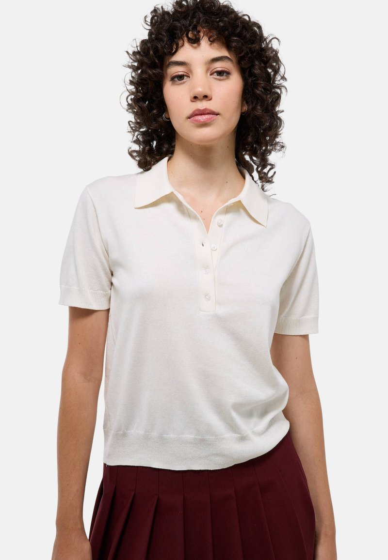 Polo à manches courtes en crème avec un col classique, patte de boutonnage à cinq boutons et ourlet côtelé. Matériau en tricot doux avec une texture lisse.