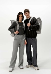 Due persone stanno insieme, indossando zaini grigi. La donna ha una maglietta nera aderente e pantaloni grigi chiari; l'uomo indossa una felpa nera e pantaloni grigi scuri.