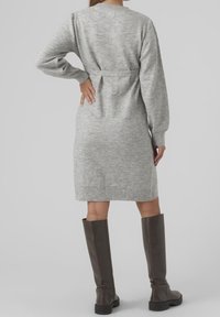 Ljusgrå stickad klänning med rund halsringning, långa ärmar och ett bälte i midjan. Kombinerad med höga, mörkbruna läderstövlar.