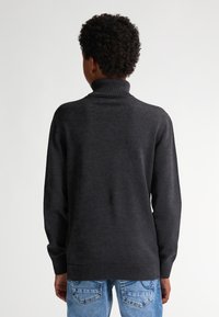 Dunkelgrauer Rollkragenpullover mit langen Ärmeln, einem gerippten Kragen und einer glatten Textur. Kombiniert mit hellblauen Jeans.