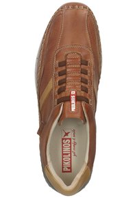Zapato de cuero marrón con textura perforada, acentos en beige contrastantes, cordones elásticos y un cuello acolchado. Logo de la marca visible en la plantilla.