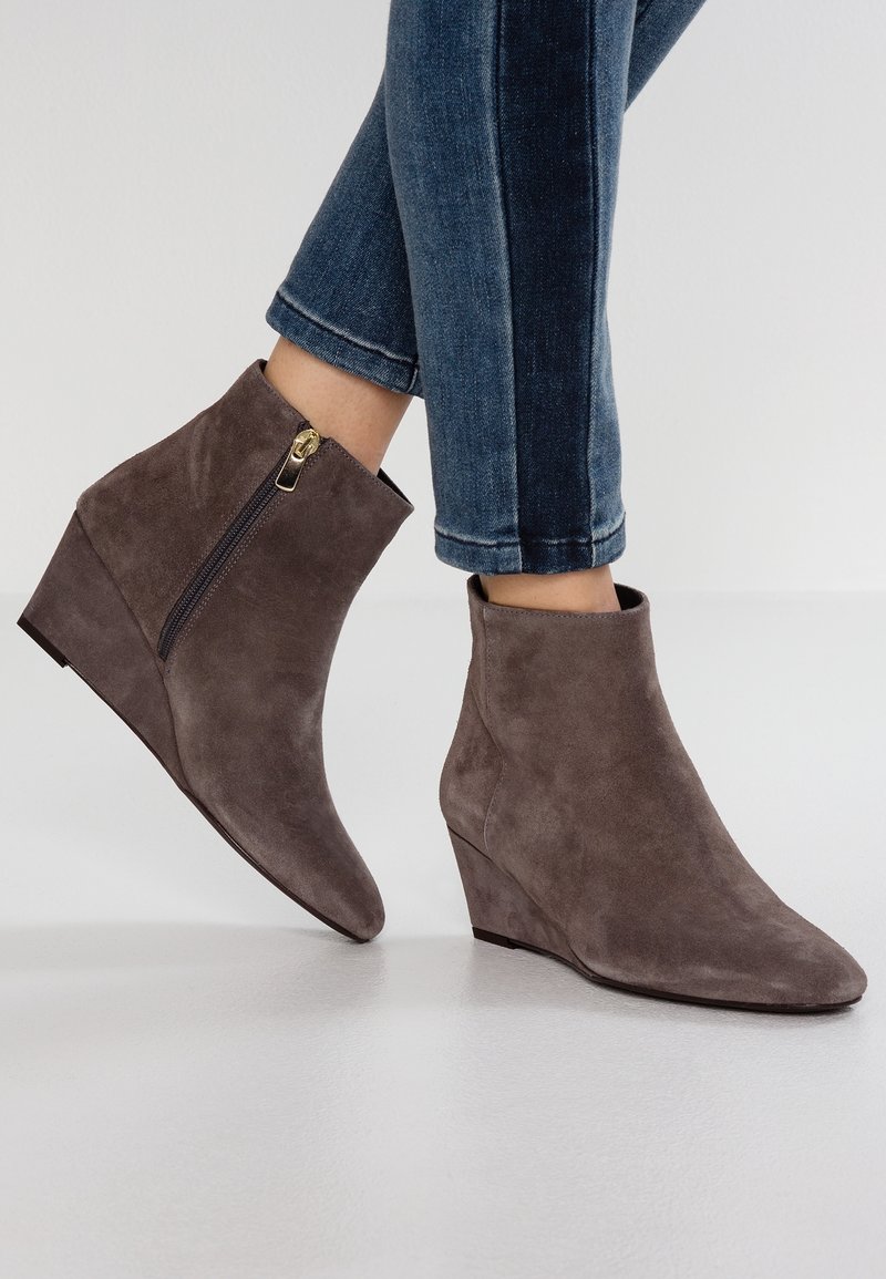 Bottines compensées en daim marron avec fermeture éclair latérale portées avec un jean skinny bleu foncé retroussé sur un fond clair uni.